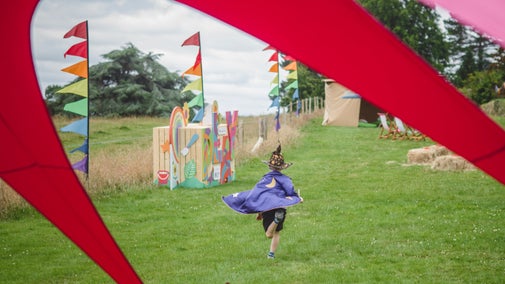A little wizard runs amongst the festival flags at the Summer of Play, Killerton, Devon